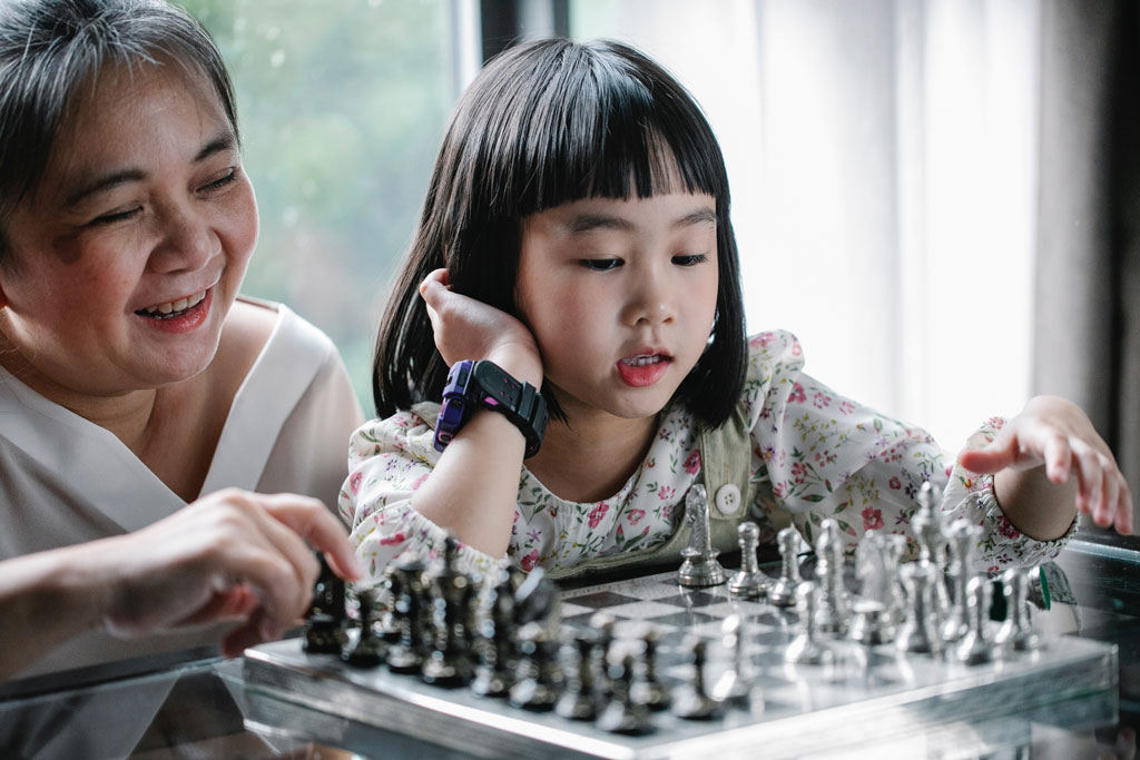 Older woman teaching her granddaughter chess